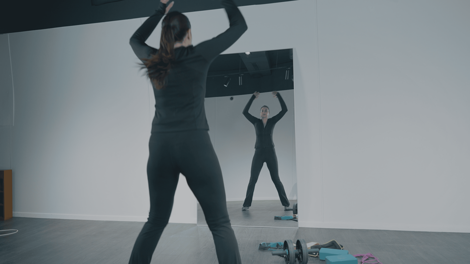 Femme faisant des jumping jacks face au miroir Plumi dans un studio de fitness